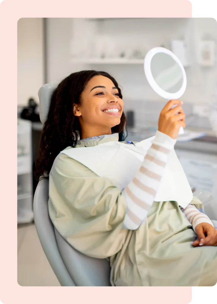 Smiling dental patient holding a mirror while checking her bright smile in a modern dental clinic